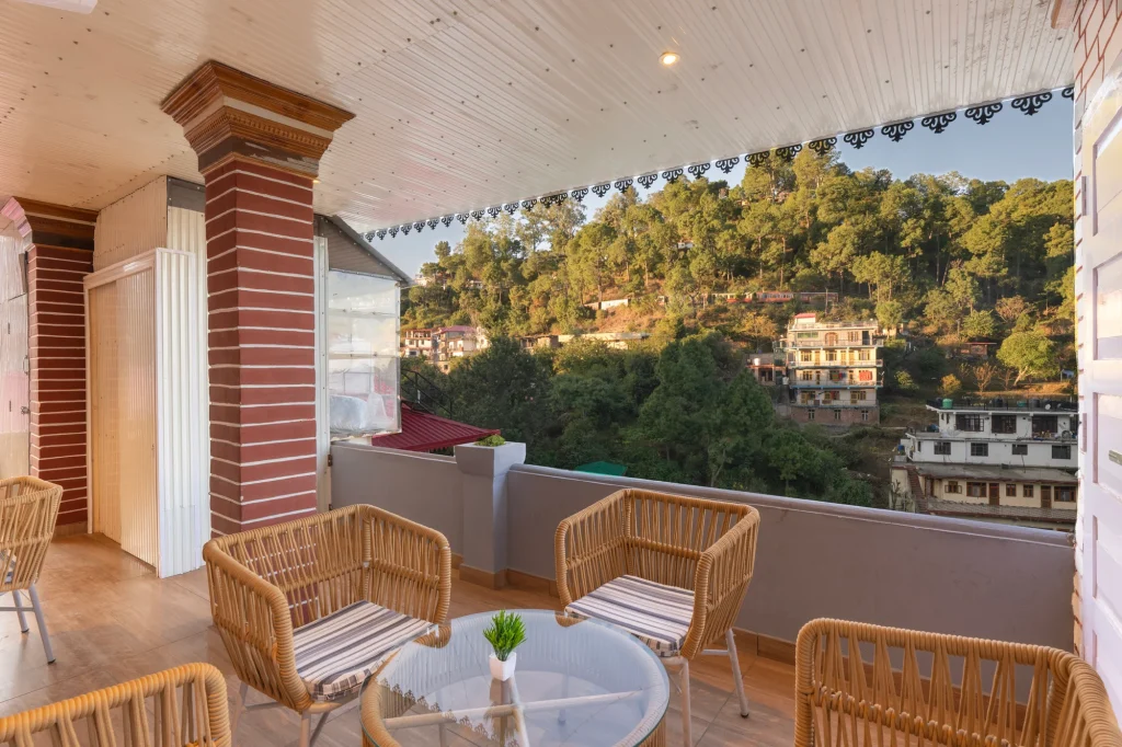 Villa balcony with wicker chairs overlooking green Kasauli hills at FarmVille
